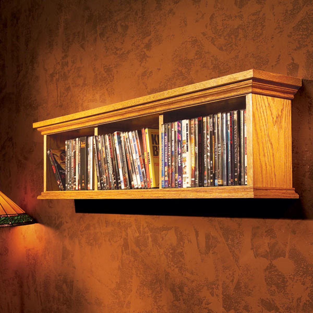 Wooden shelf holds neatly arranged DVDs against a textured brown wall, illuminated by a stained glass lamp nearby.