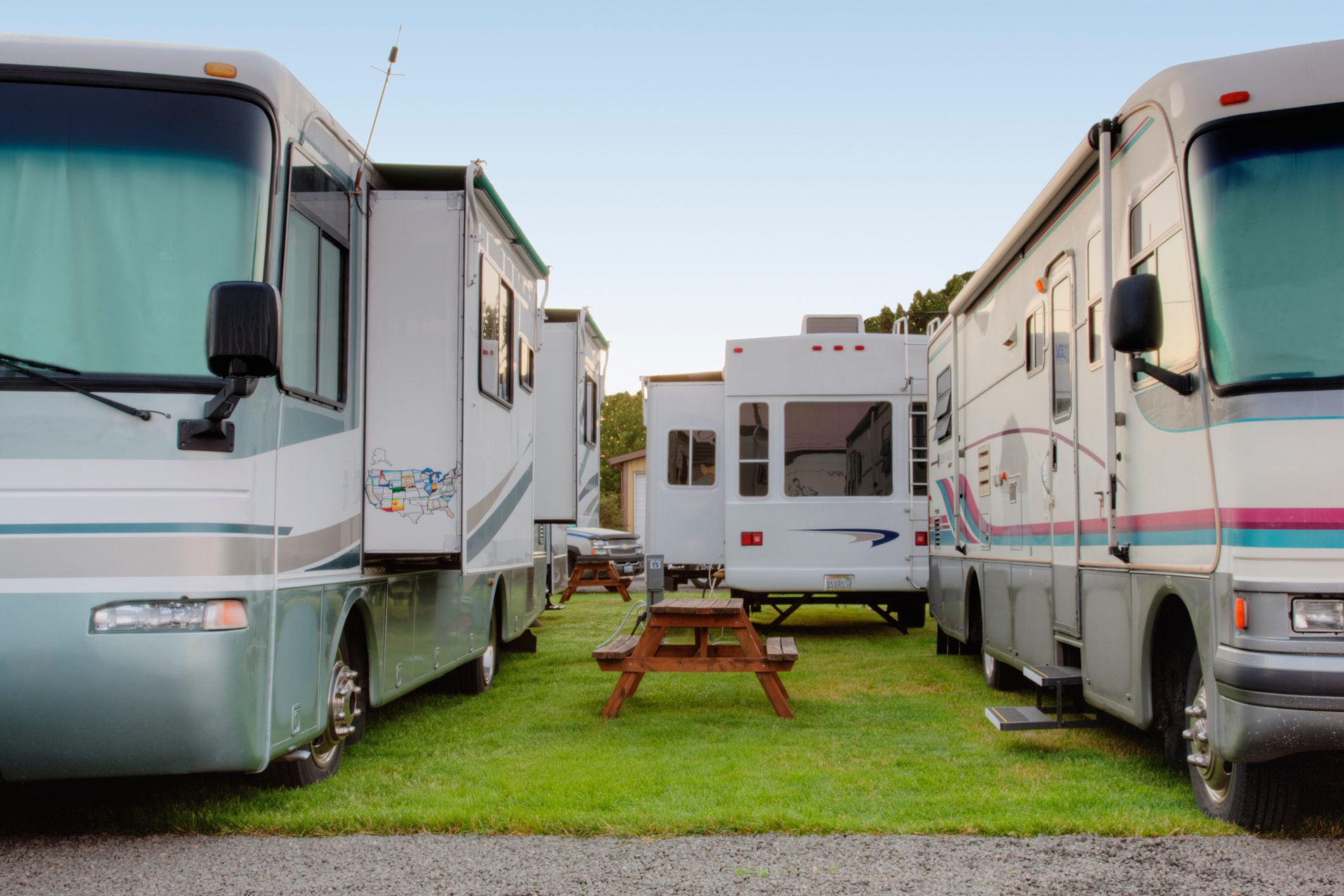 Two R.V.s are parked on grass with a picnic table between them, creating a cozy camping setting.