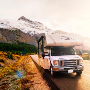 RV parked along a scenic mountain road, with autumn foliage and snow-capped peaks in the background under a bright sky.