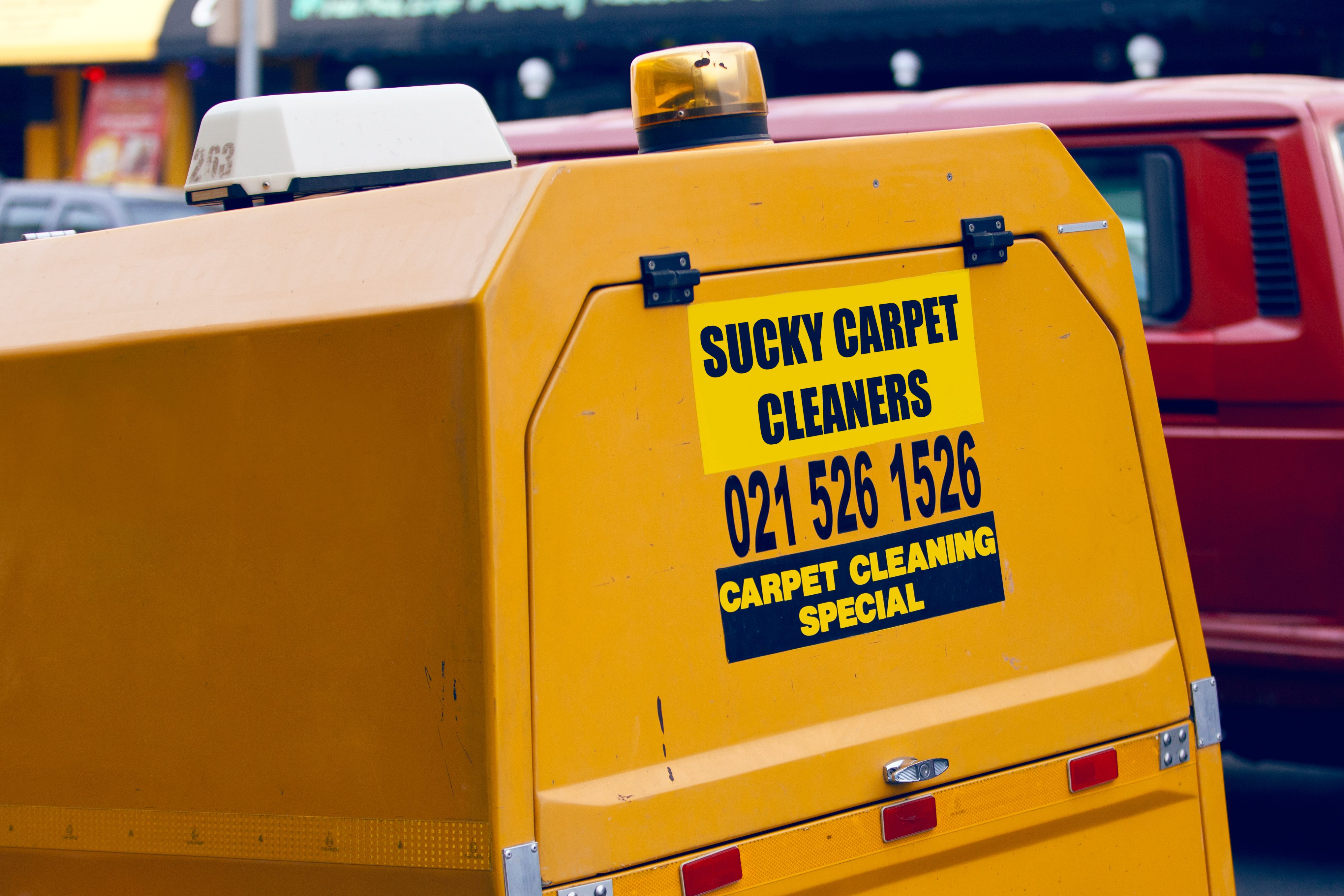 Yellow cleaning vehicle displays "Sucky Carpet Cleaners, 021 526 1526, Carpet Cleaning Special" in an urban environment.