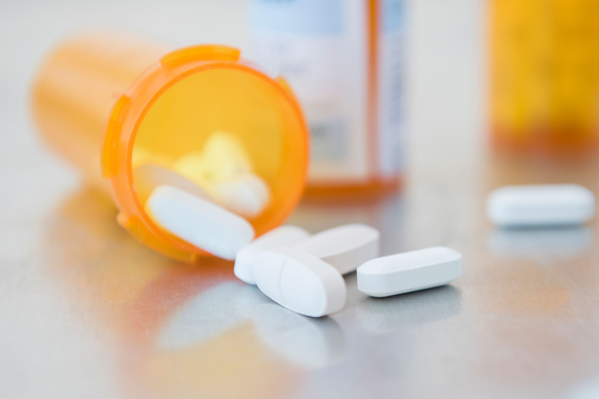 White pills spilling from an orange pill bottle onto a smooth, reflective surface.