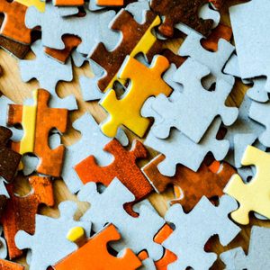 Puzzle pieces scattered, various colors, lying on a wooden surface in disarray.