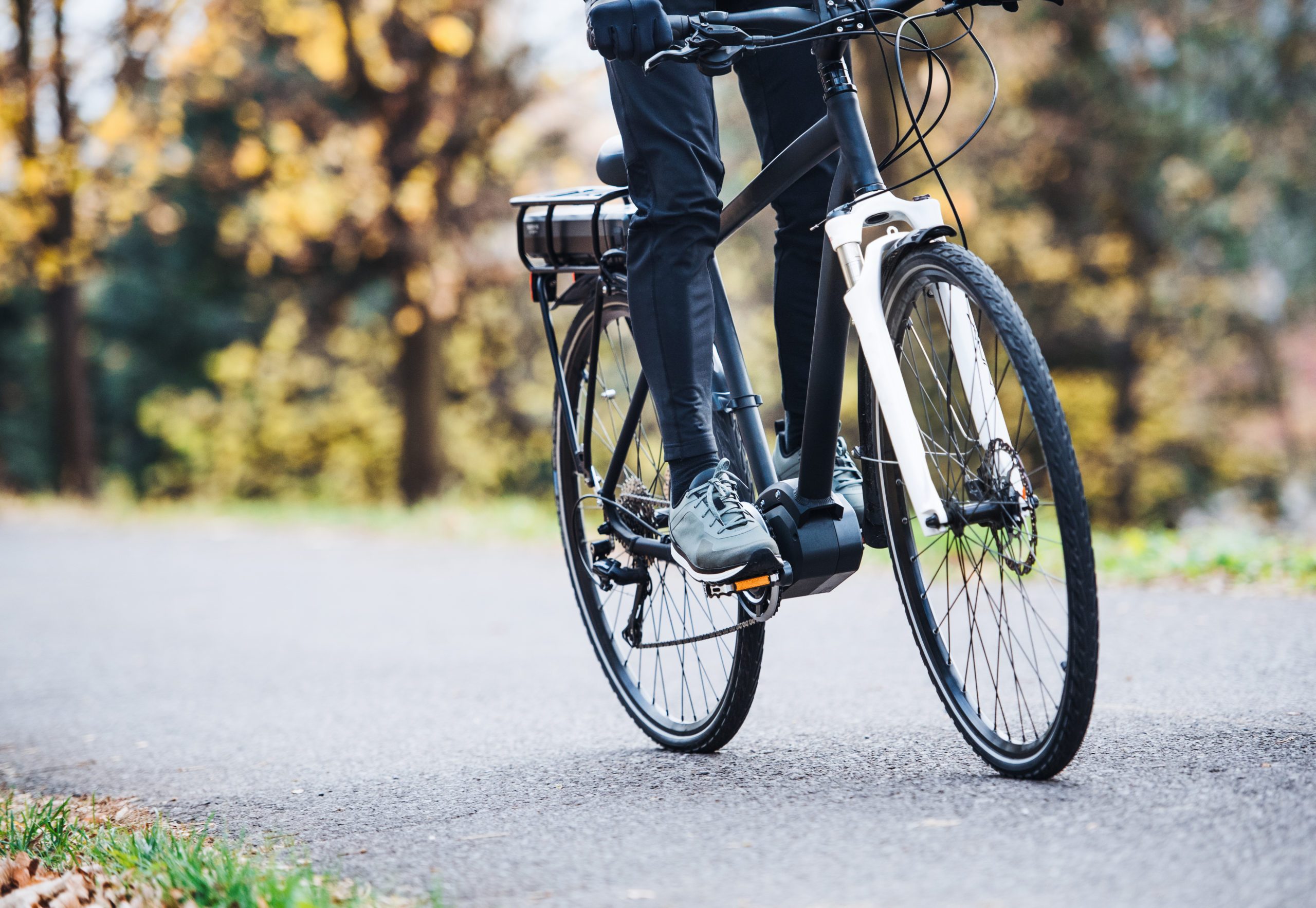 A bicycle is ridden along a paved path, surrounded by blurred autumn trees. The rider wears dark clothing and green shoes.