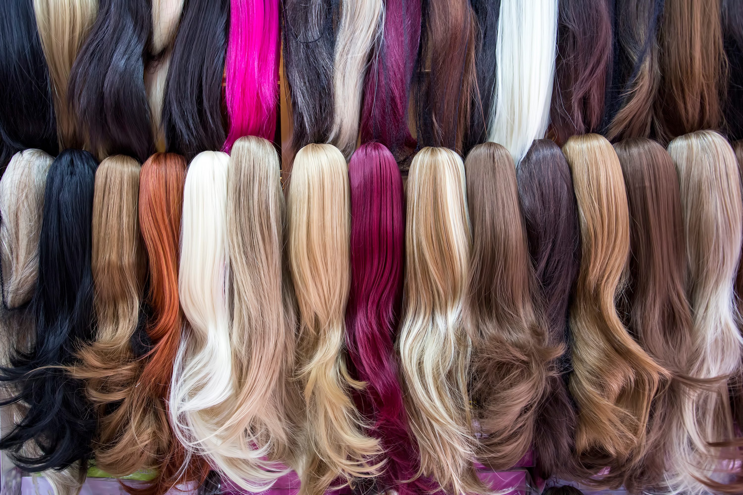 Wigs hang in vibrant shades, creating a colorful display on a shop wall.