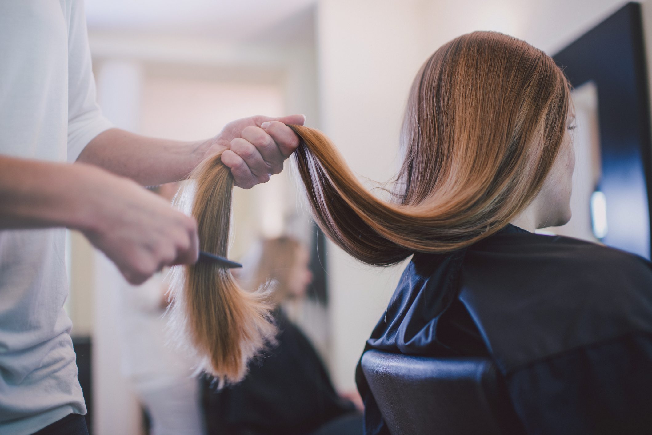 A person combs long hair, preparing to cut it, inside a hair salon.