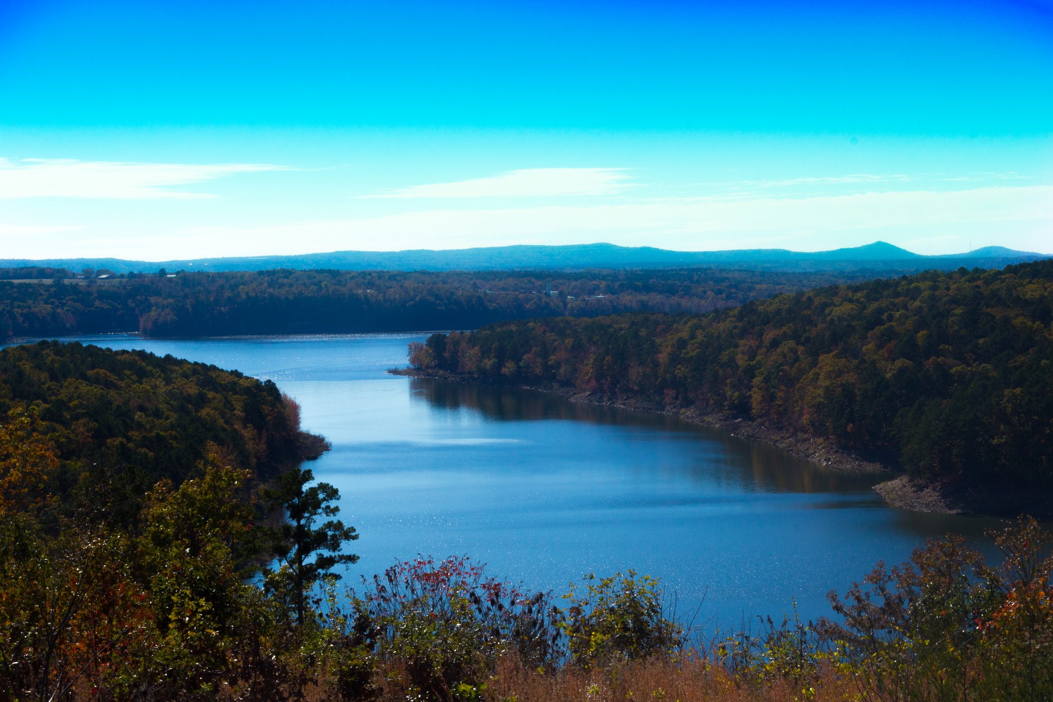 A wide river winds through forested hills under a clear blue sky, creating a serene and scenic landscape.