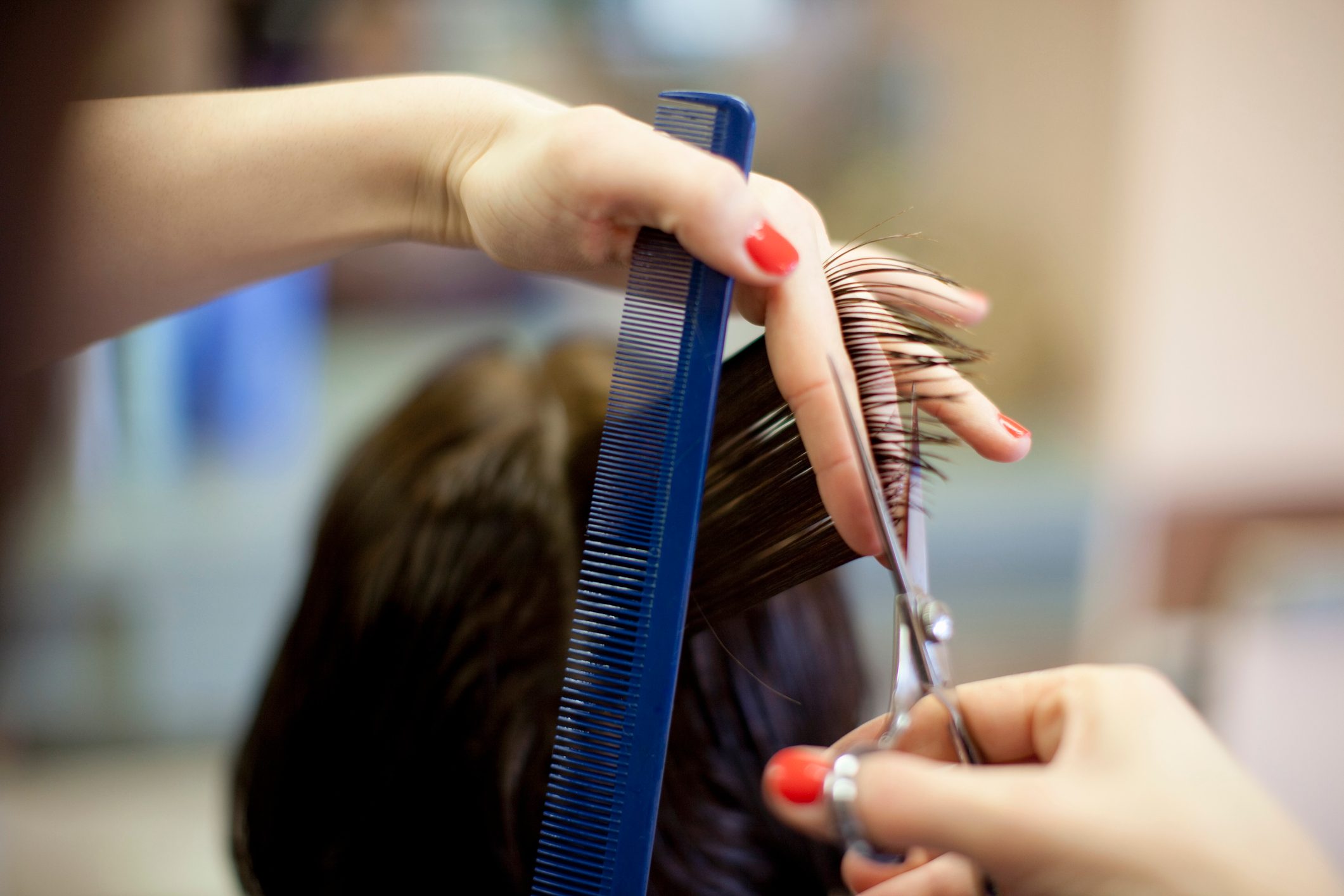 Hands cut hair using scissors and a blue comb, focusing on a haircut in a salon setting.