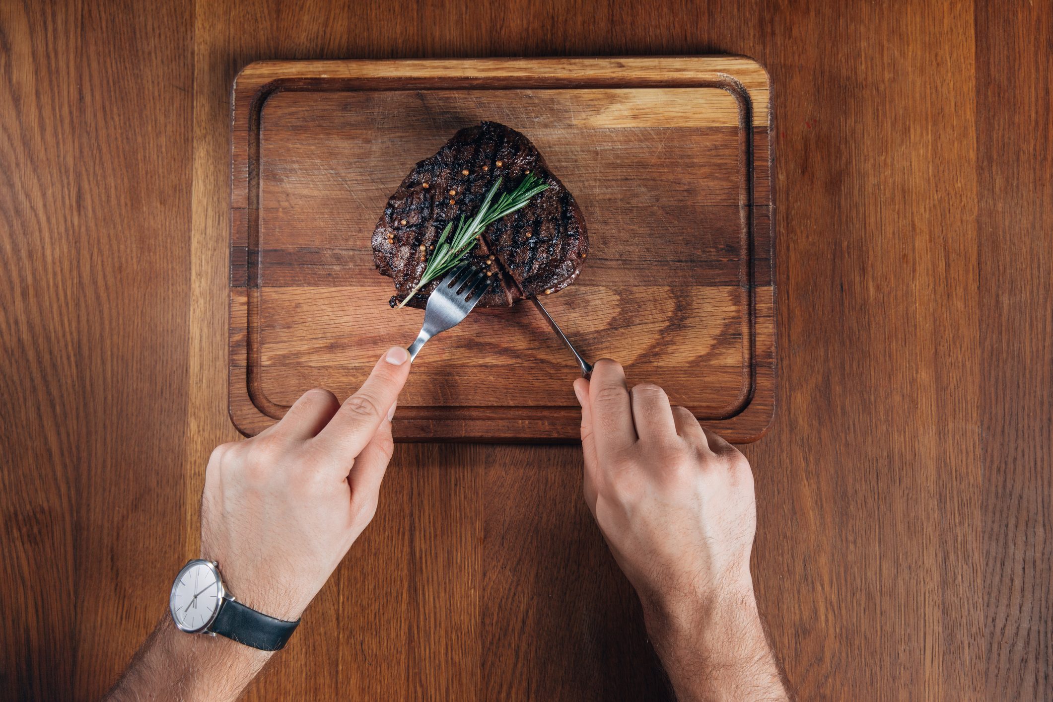 cropped shot of man cutting grilled steak on wooden board