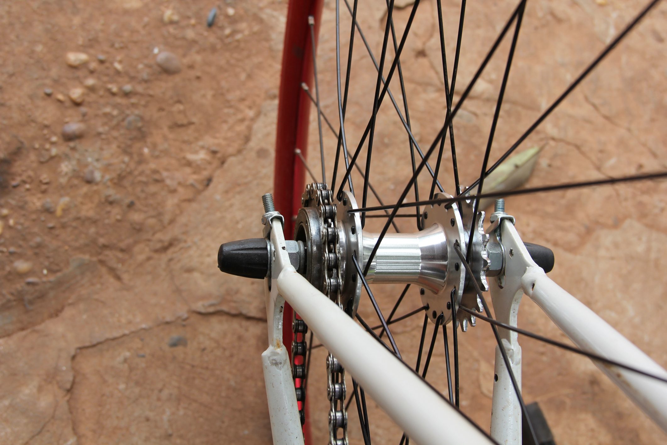 Bicycle wheel with black spokes rotates, mounted on white frame; visible red tire and metallic hub on a textured brown ground.