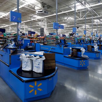 Checkout counters display bags, registers, and products in a brightly lit supermarket aisle, featuring overhead signage with numbers for organization.