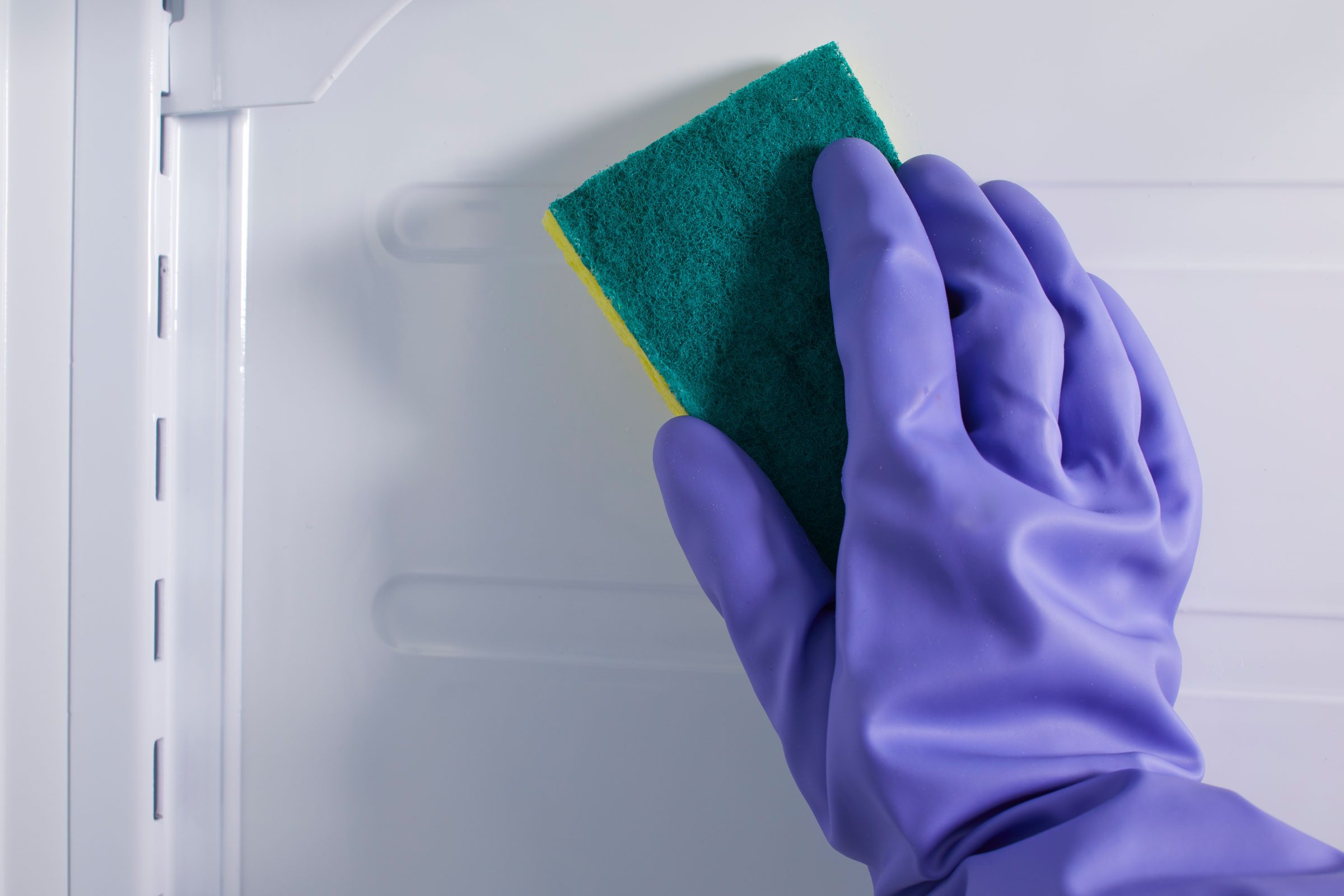 hand holding sponge cleaning the inside of a refridgerator