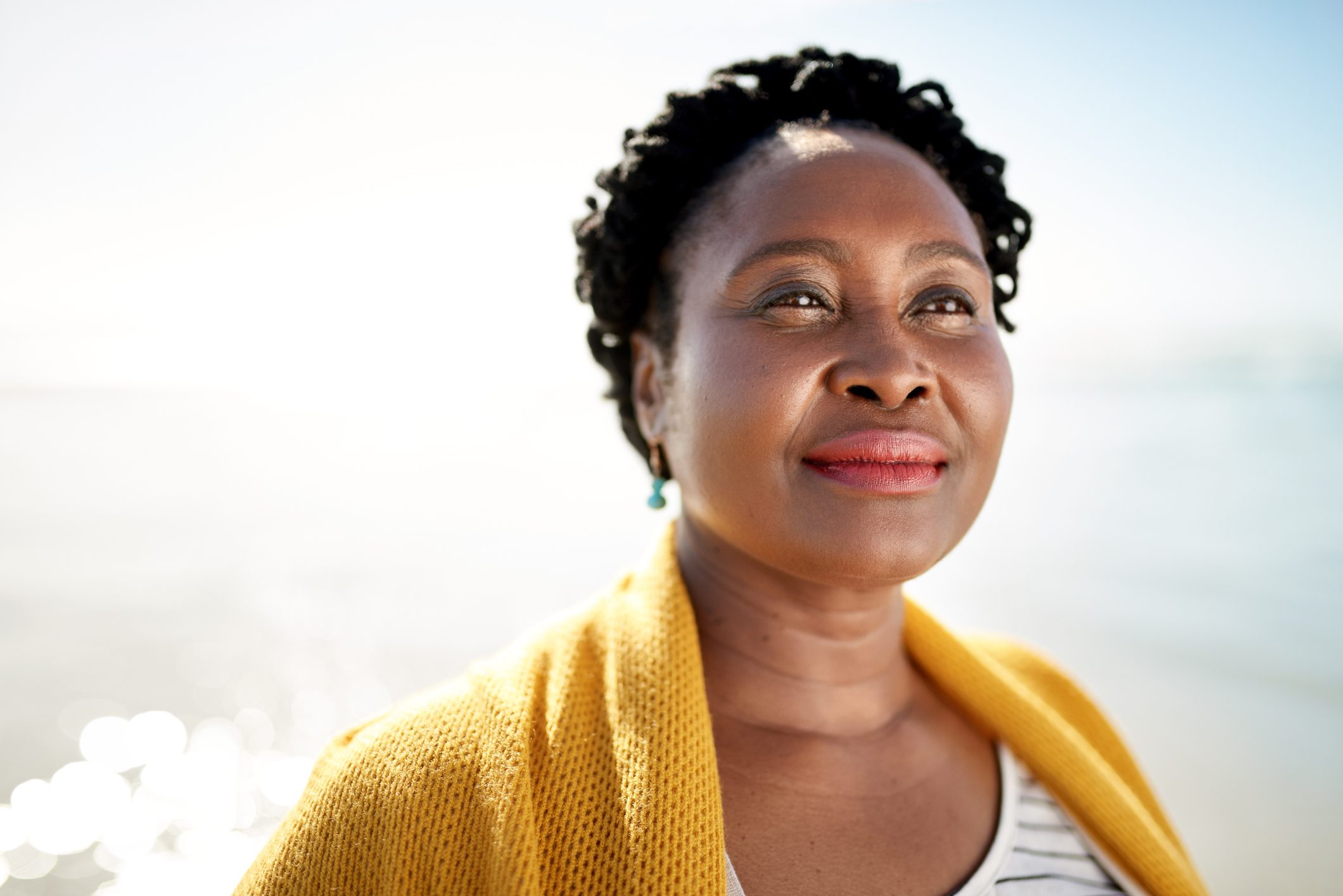 A woman stands gazing upward, wearing a yellow shawl, with a serene beach background.
