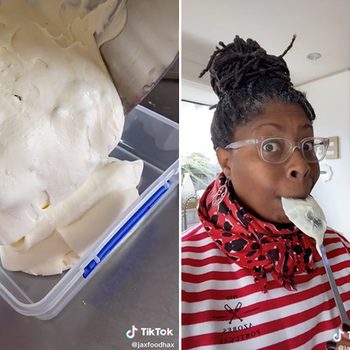 A person licks a spoon in a kitchen, wearing glasses, a patterned scarf, and striped shirt. Creamy substance poured into a container.