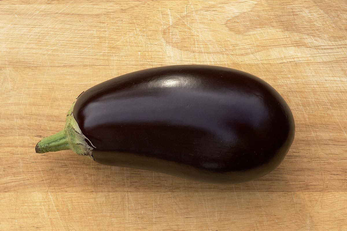 Eggplant resting on a wooden cutting board, showcasing its glossy purple skin and green stem.