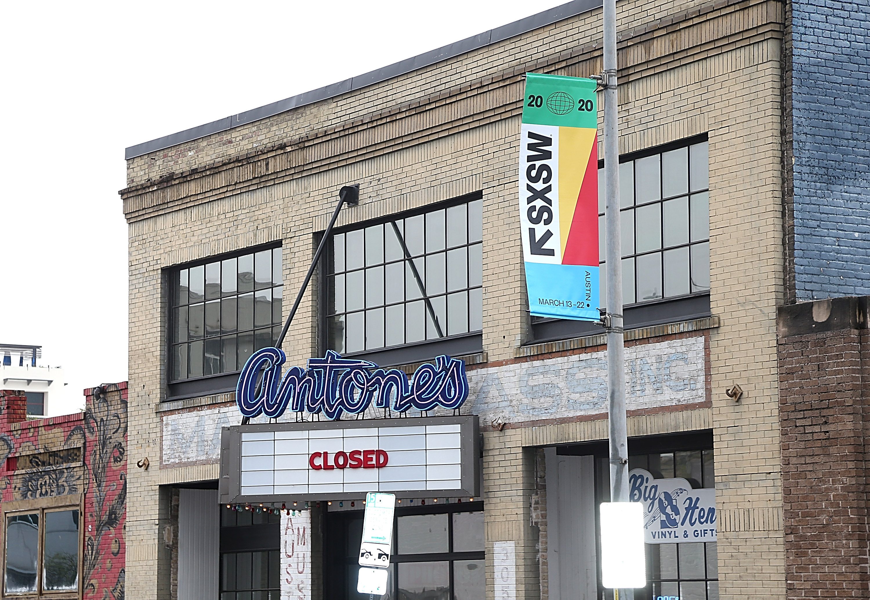 The sign reads "Antone's" with "CLOSED" beneath; a colorful SXSW 2020 banner hangs nearby on a brick building in an urban setting.
