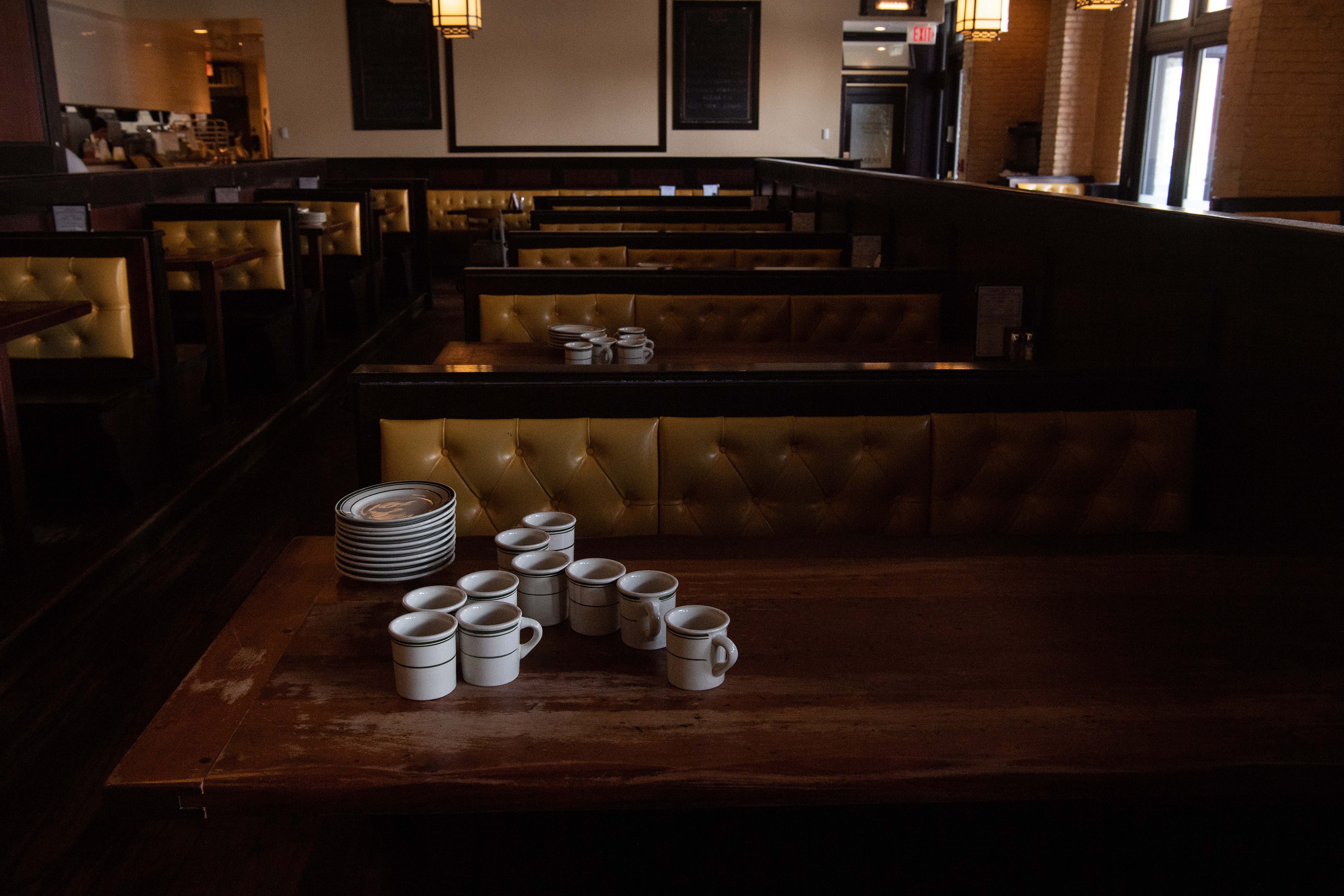Mugs and plates rest on a wooden table in a dimly-lit restaurant with yellow cushioned booths lining the walls.