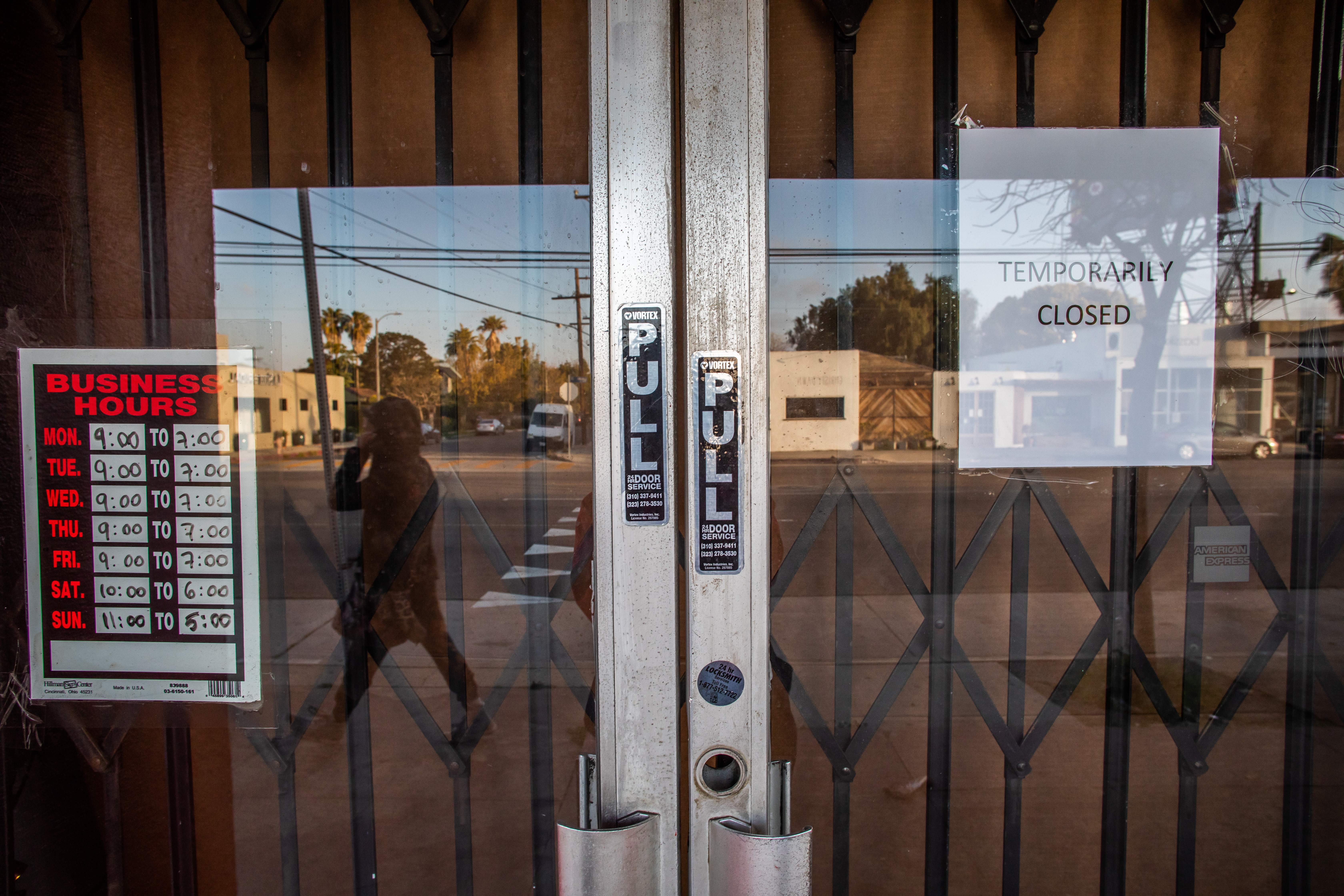 Glass doors display "Temporarily Closed" and business hours, with street reflection visible in a sunny urban setting.
