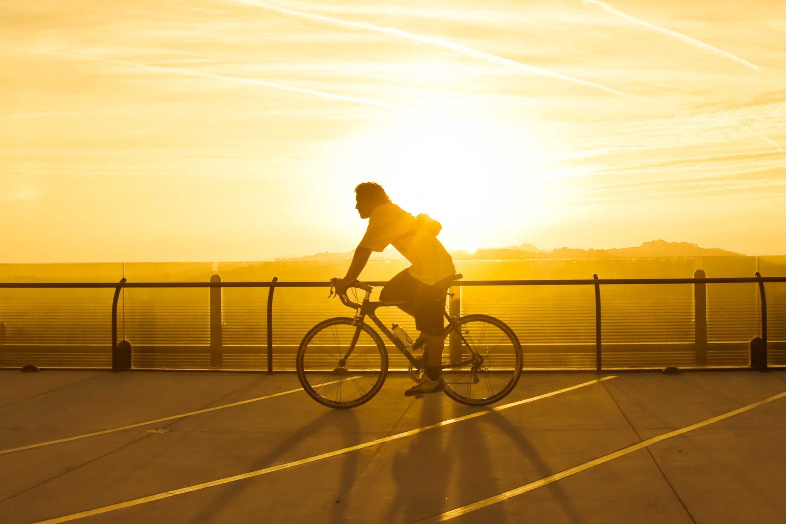 Silhouette of a cyclist riding, with the sun setting in the background, casting long shadows on the open terrace.