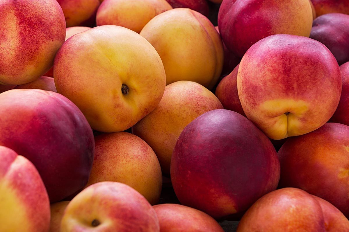 Peaches are piled together, exhibiting vibrant red and yellow hues, creating a fresh and colorful display.