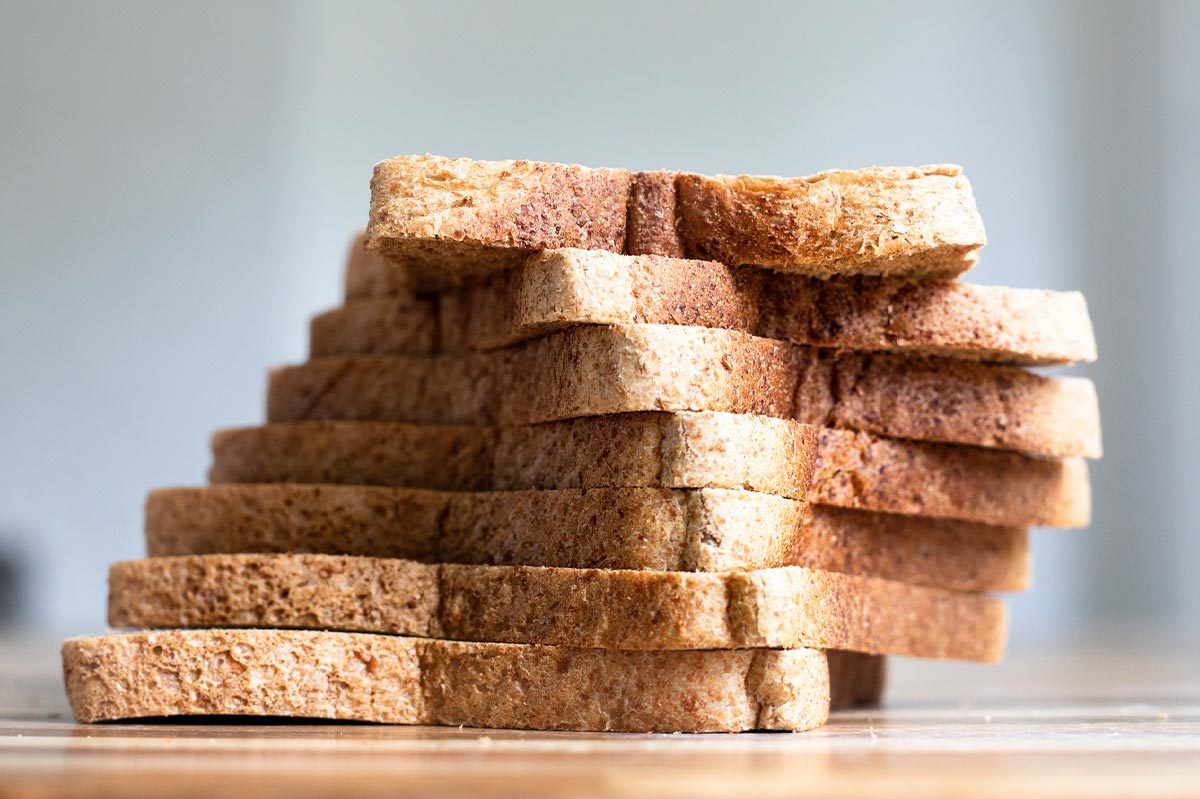 Sliced bread stacked into a leaning tower, resting on a wooden table in a softly lit room.