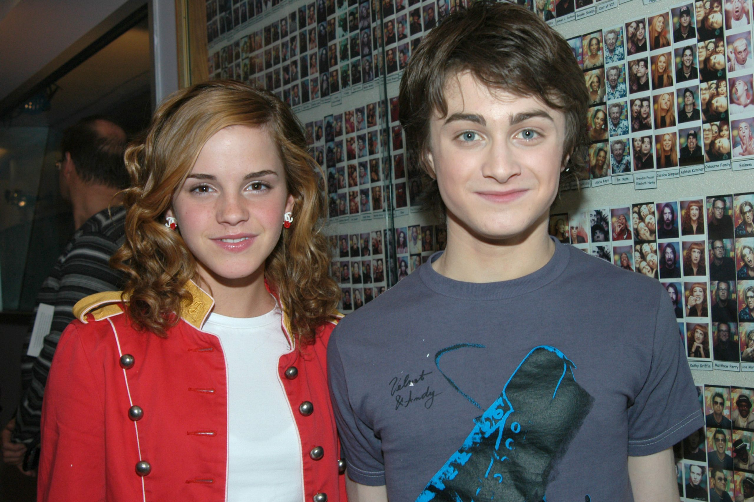 Two young people stand smiling; walls display countless small photographs.