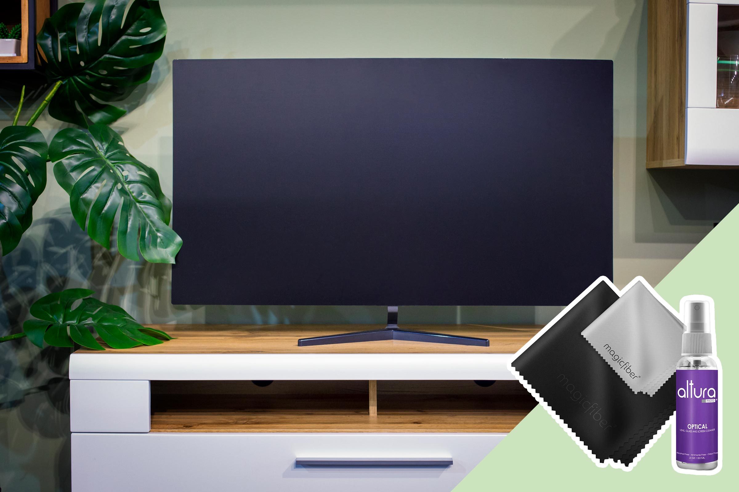 A television rests on a wooden stand beside large green leaves, accompanied by cleaning cloths and spray in the foreground.