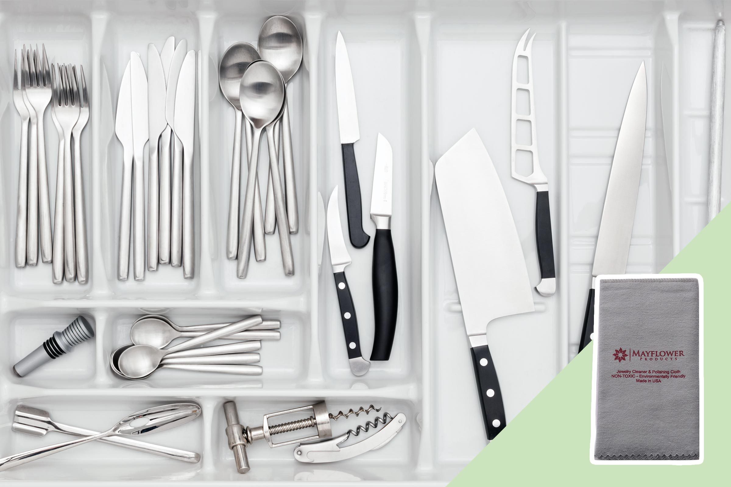 Cutlery and knives neatly arranged in a white drawer organizer; a corkscrew, tongs, and spoons included. Text reads "Mayflower Products" on a cloth.