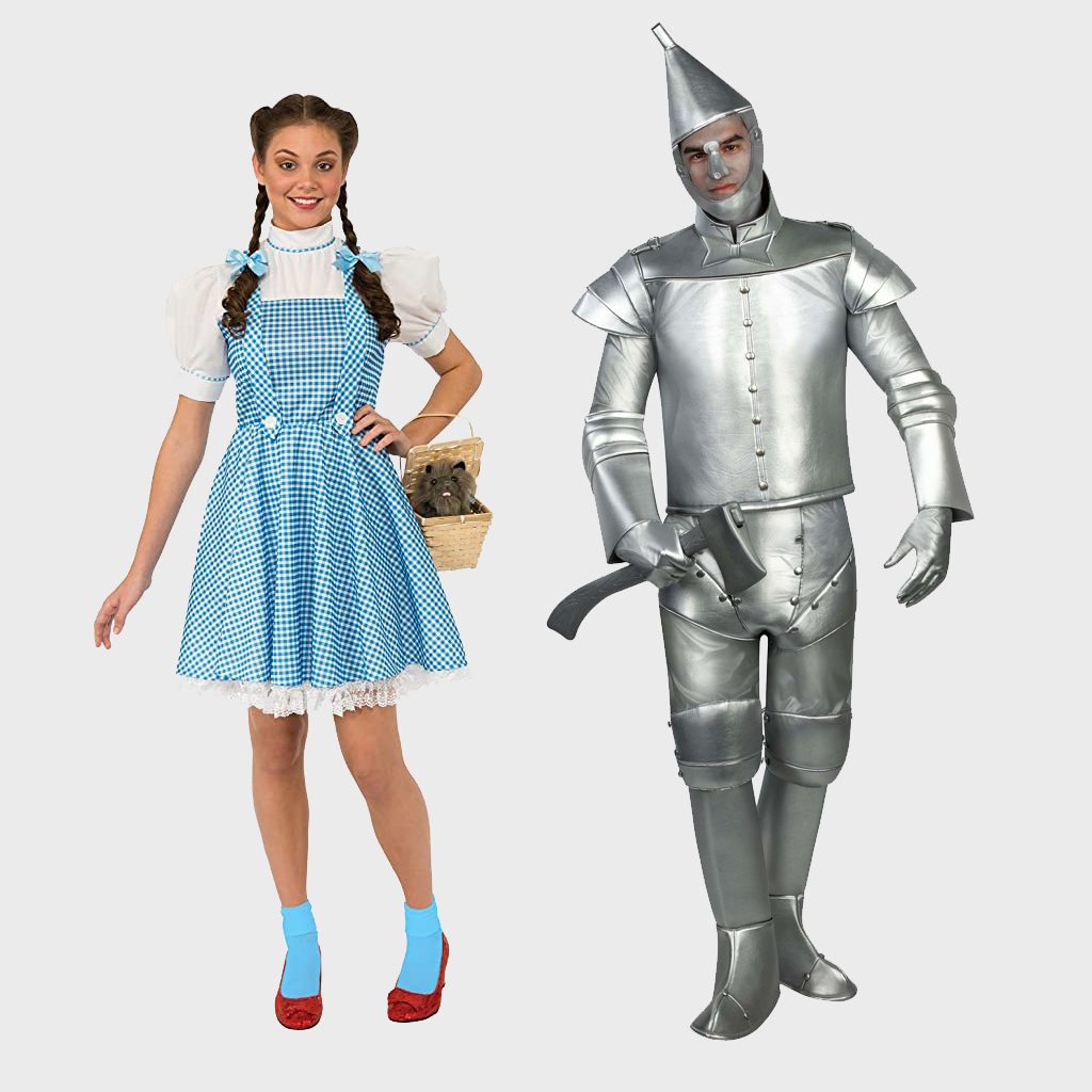 A woman and man wear costumes. She wears a blue dress holding a basket; he is in a silver, tin-man suit with an axe.