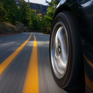 Car wheel spinning on a winding road, surrounded by trees and hills.