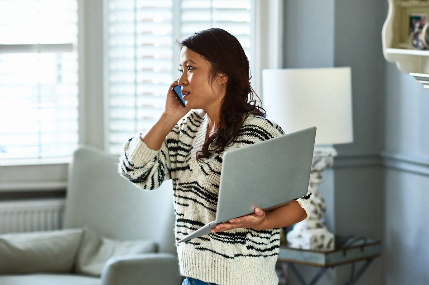 Woman holding laptop and listening on smartphone