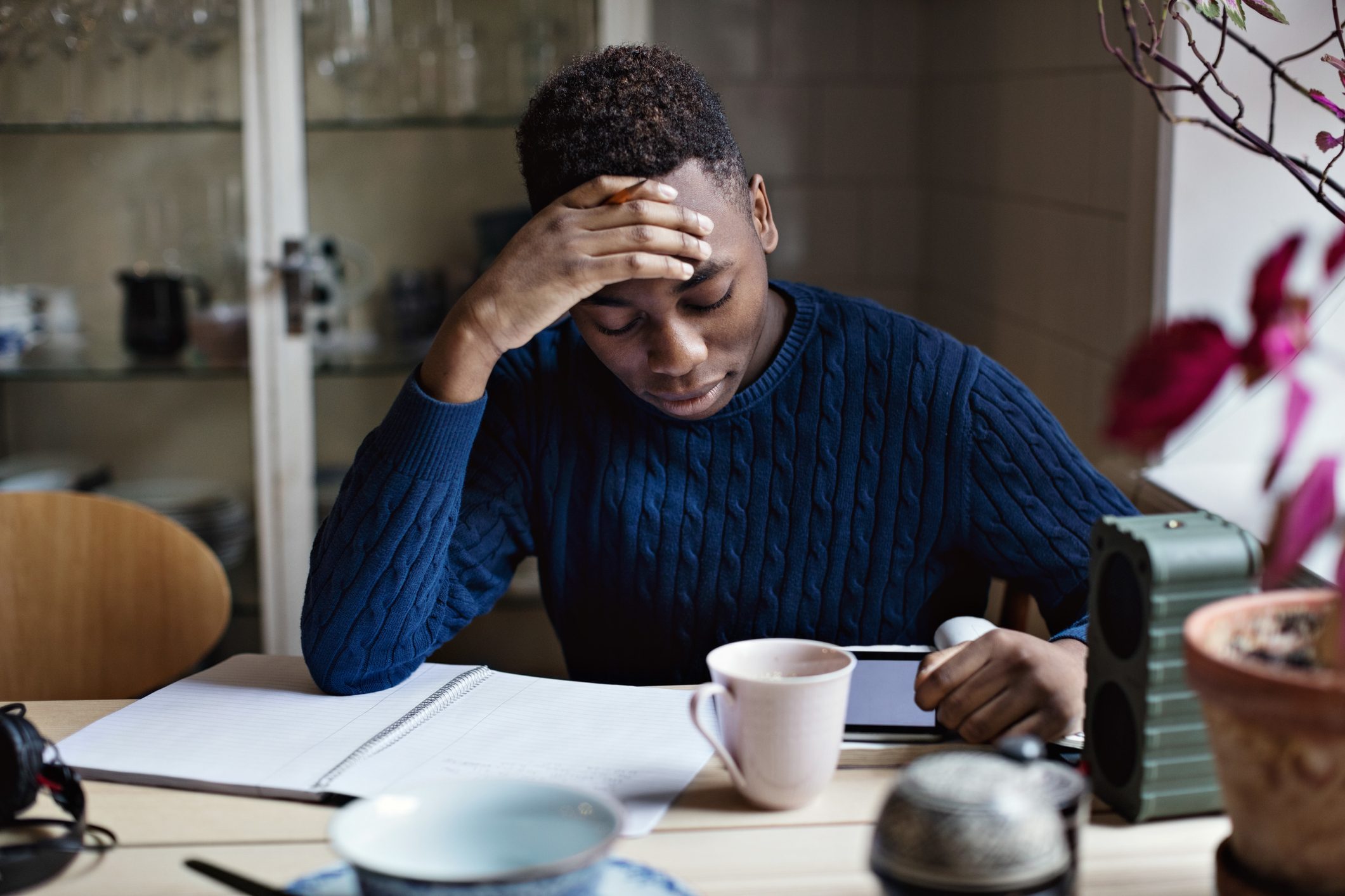 Worried teenage boy with head in hand studying at home