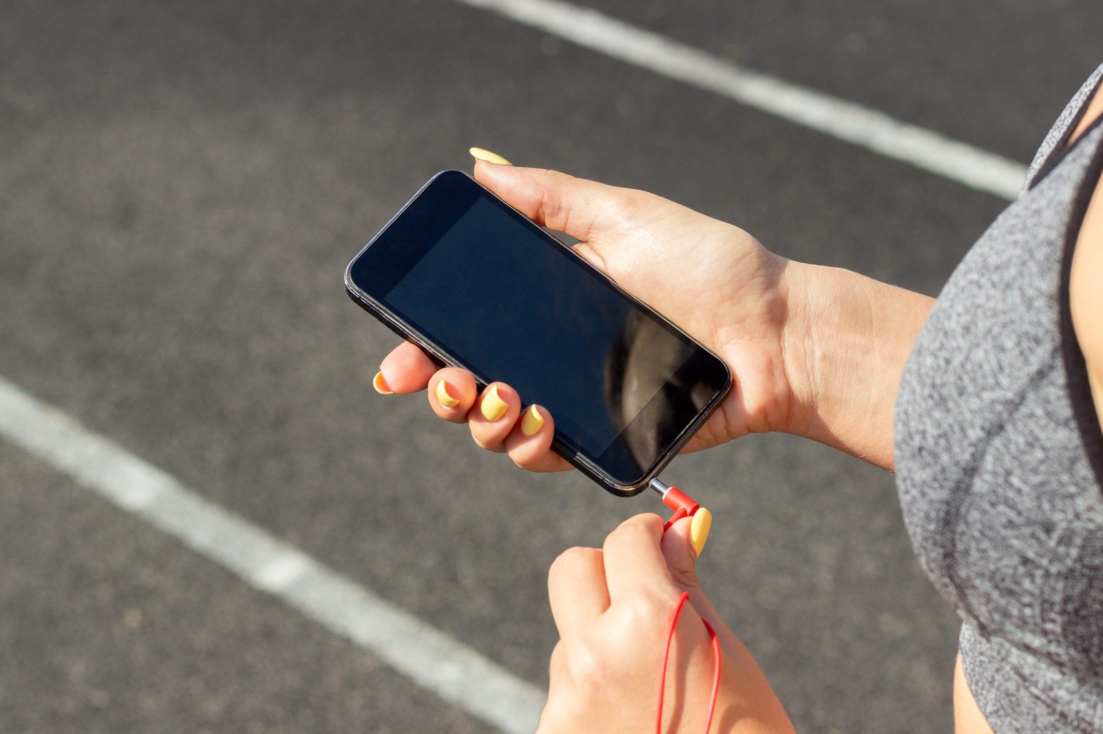 Midsection Of Woman Plugging Headphones In Smart Phone On Running Track