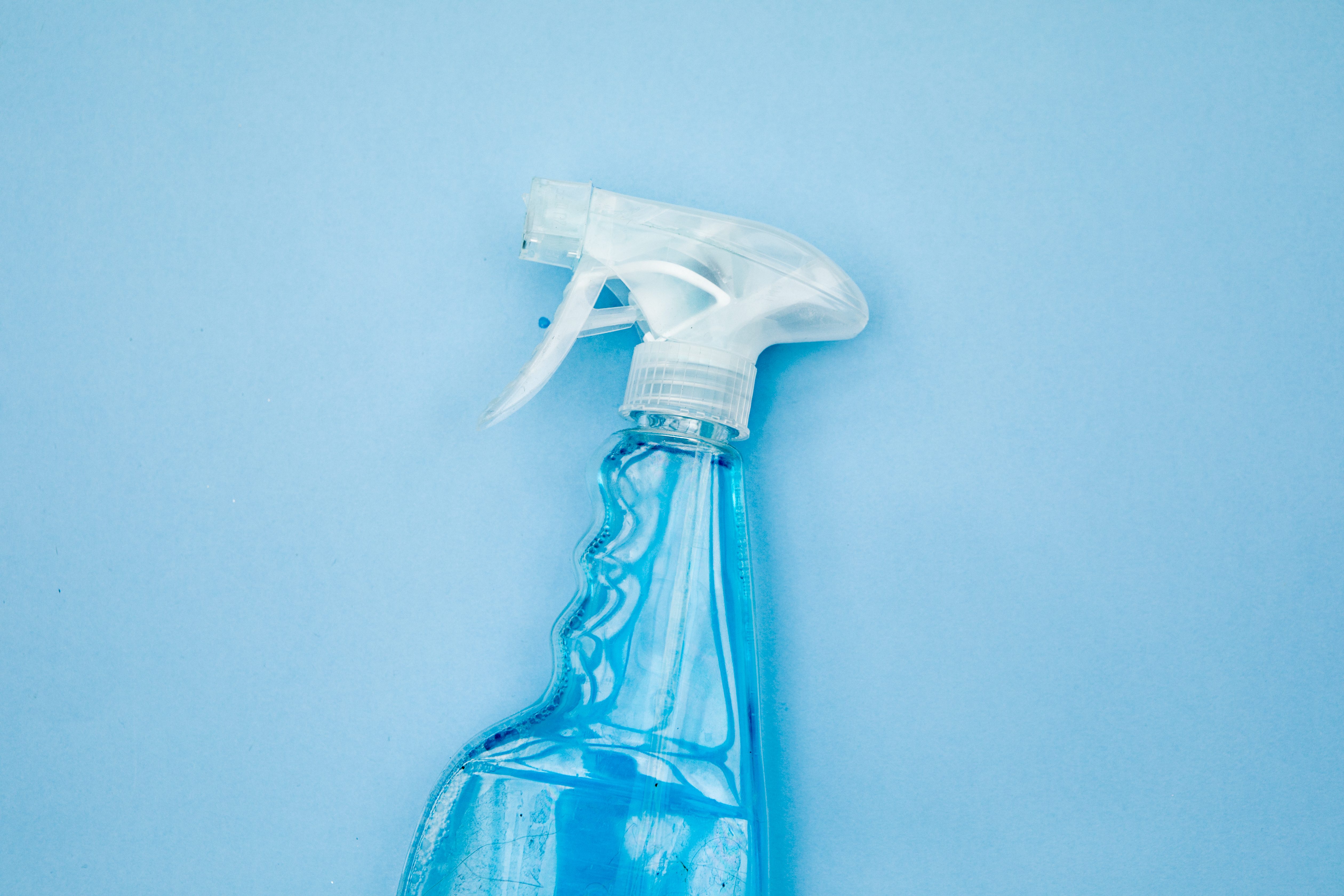 Clear spray bottle containing blue liquid, resting on a solid light blue background.