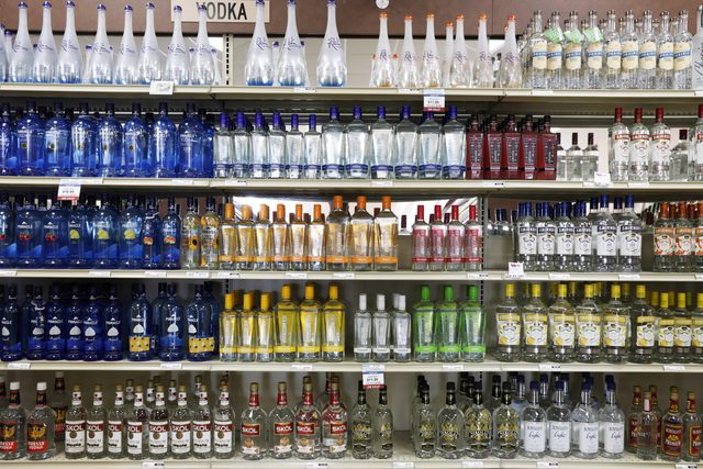 Bottles are standing on a store shelf in neat rows, displaying various vodka brands with colorful labels and price tags in a liquor store.