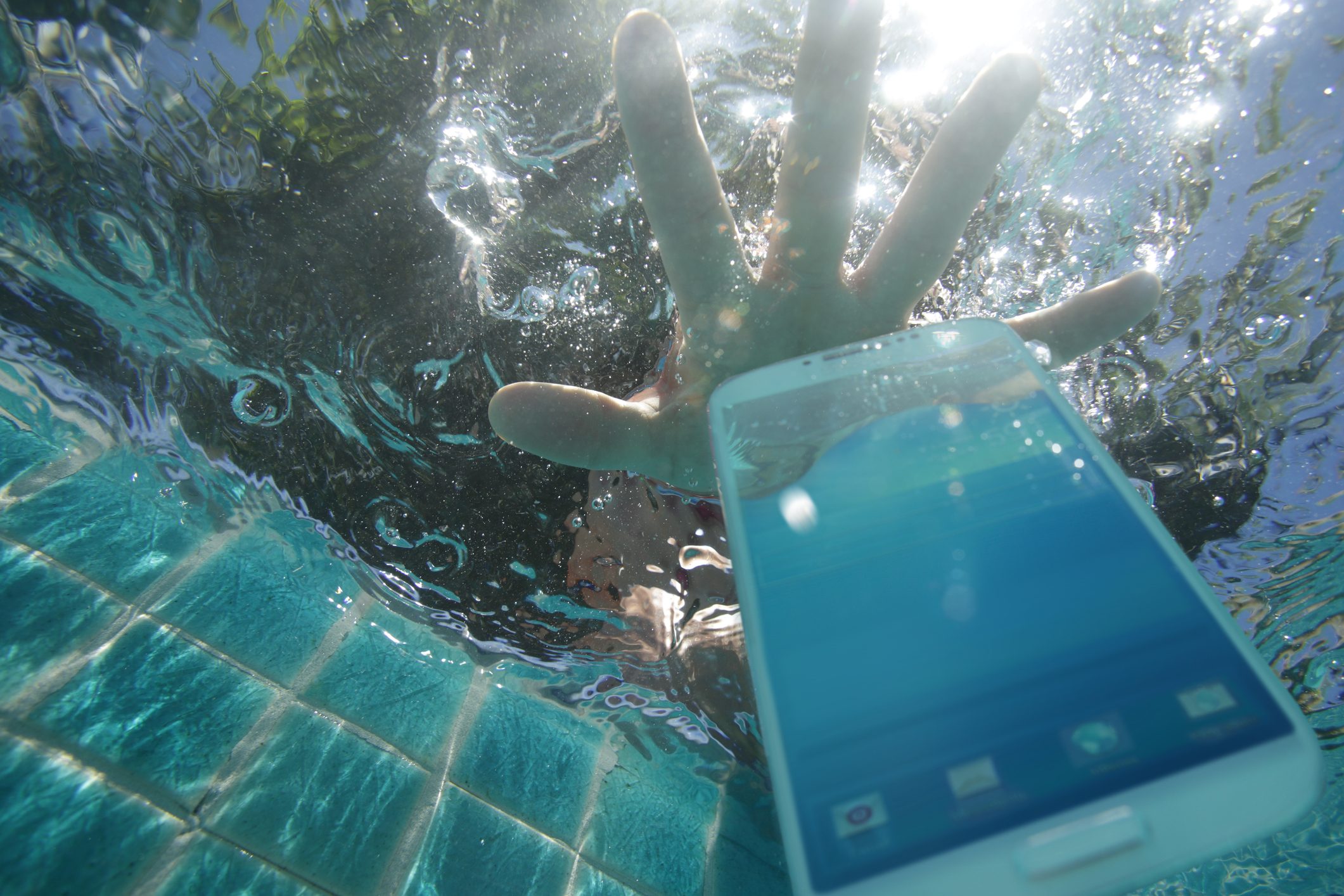 Hand reaching for phone dropped in pool