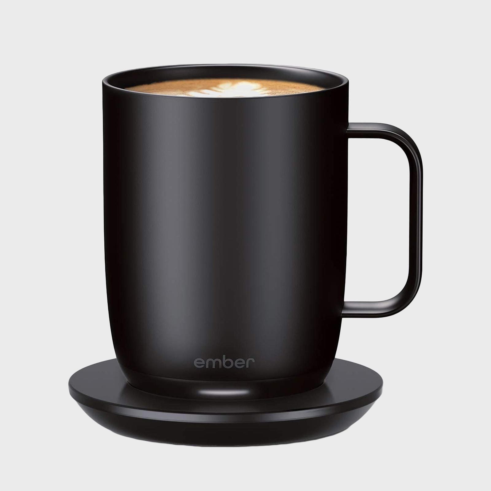A black mug rests on a matching saucer. It holds a latte with foam art. The word "ember" is visible on the mug.