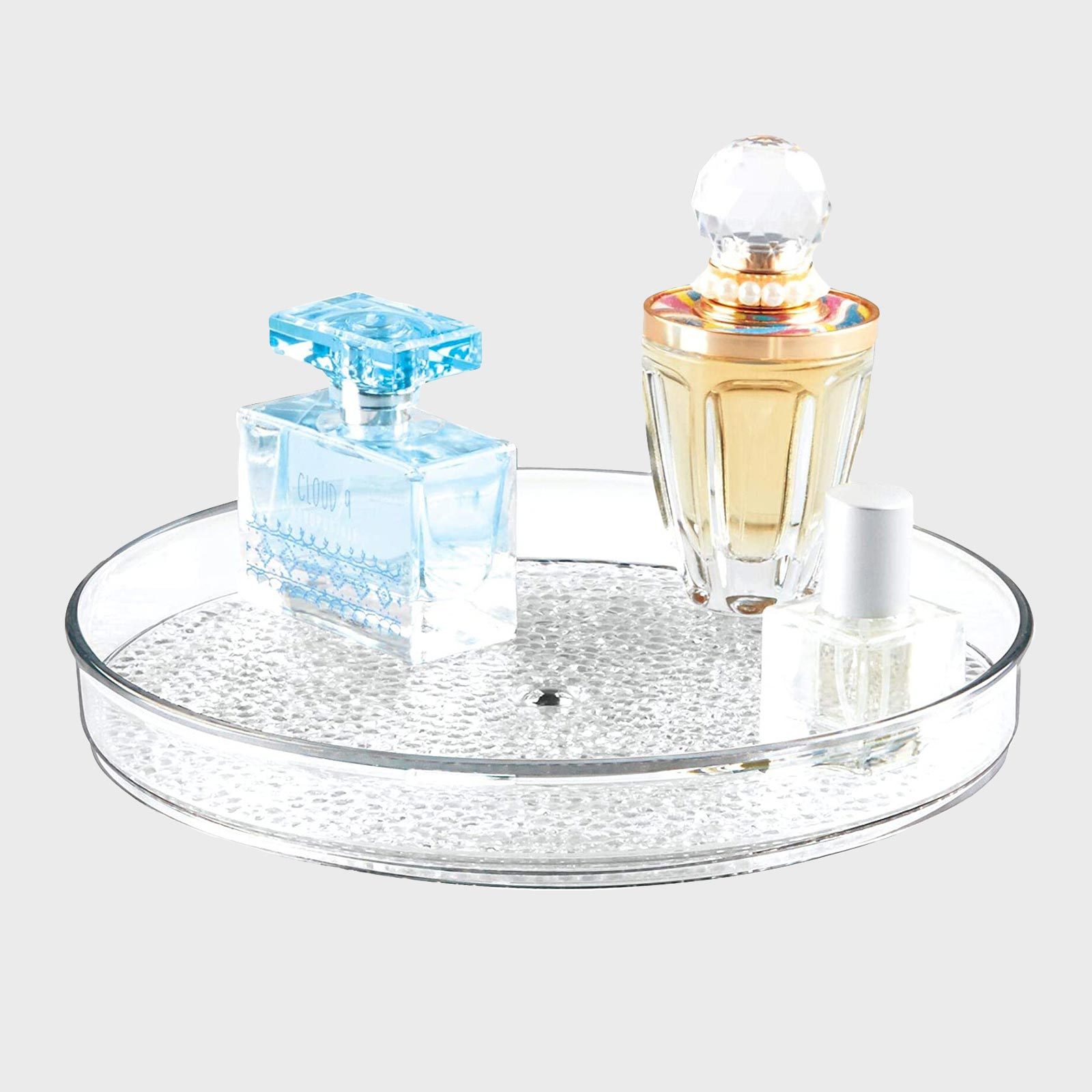 Perfume bottles sit on a round, textured, clear glass tray against a plain background.