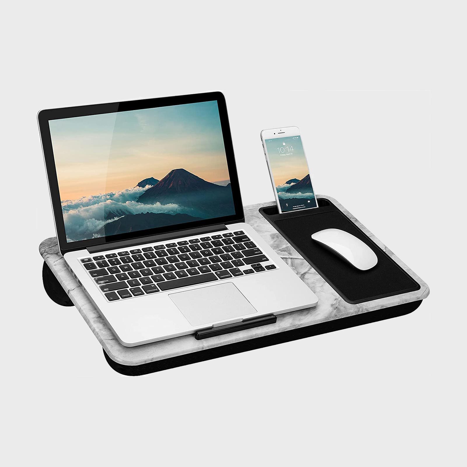 A laptop rests on a lap desk with a smartphone in a slot and a mouse on a pad, against a plain background.