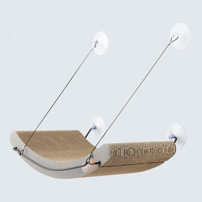 Cardboard lounging perch hangs, supported by suction cups, against a light background; used for cats.