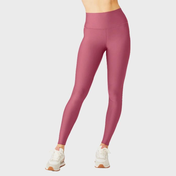 Pink leggings are being worn, with person standing, wearing white sneakers against a plain light background.