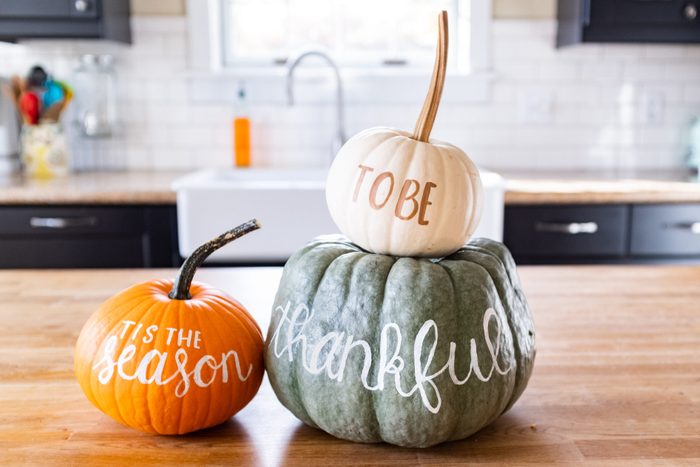 Three pumpkins sit on a kitchen counter, each with handwritten words: 