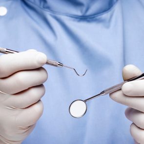 Gloved hands hold dental instruments in a clinical setting.