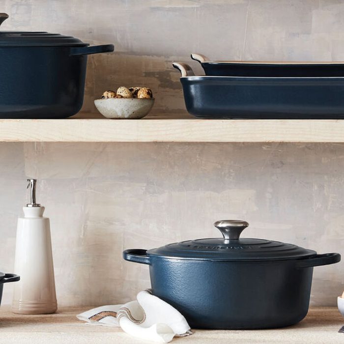 Cookware sits idle on wooden shelves in a rustic kitchen, with neatly stacked pots and a cloth beside a bottle.