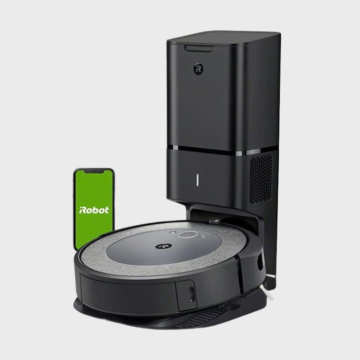 Robot vacuum charges at docking station with smartphone displaying 