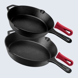 Two black cast iron skillets stacked, each with red silicone handle covers in a kitchen setting. Handle covers display the brand 
