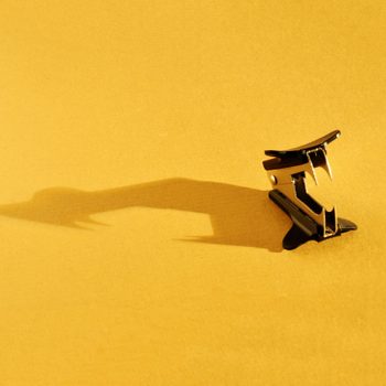 Staple remover casting a shadow on a flat, yellow surface, resembling a bird in flight.