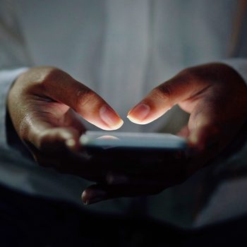 Hands typing on a smartphone, glowing in the dark, creating an illuminated contrast against a dim background.