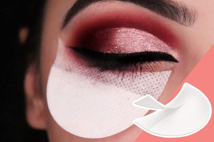 Eye with glittery pink eyeshadow, wearing eyeliner, and a white makeup shield pad underneath, against a pink background.