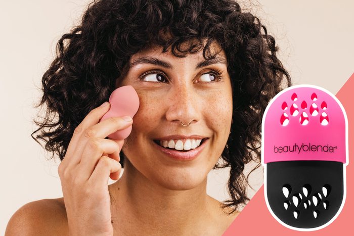 Woman smiling, applying makeup with a pink sponge. The background is simple, and a product with 