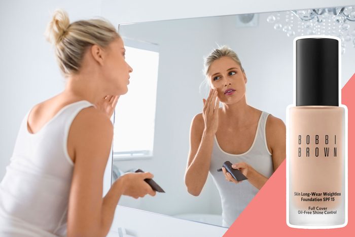 A woman applies makeup in front of a mirror, holding a compact. The room is bright, and 